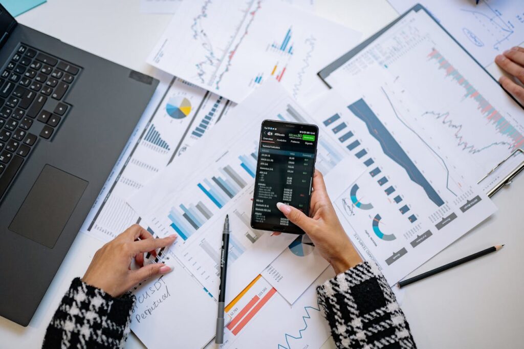 A person holding a black android smartphone rests their hands on a table filled with data charts