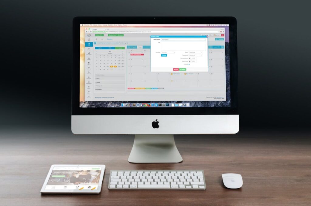 An iMac, a magic keyboard and mouse, and a tablet on a wooden table